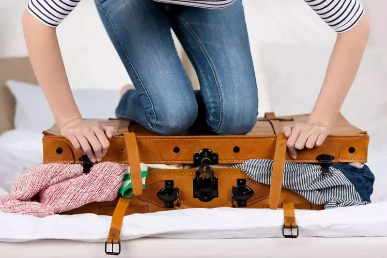 Woman holding down suitcase to close